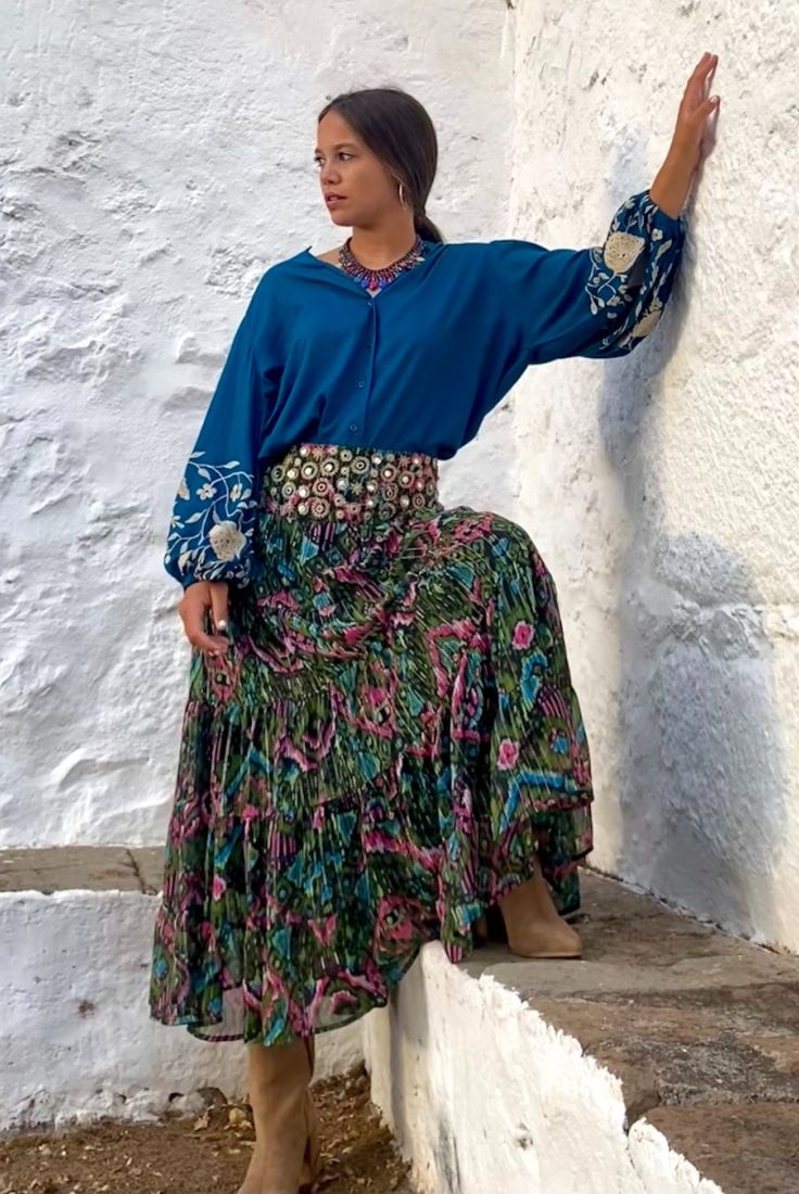 Mujer joven vestida con blusa azul con bordados blancos en mangas, y falda de vuelo de estampados étnicos multicolor, con cintura bordada con espejitos, de estilo bohemio