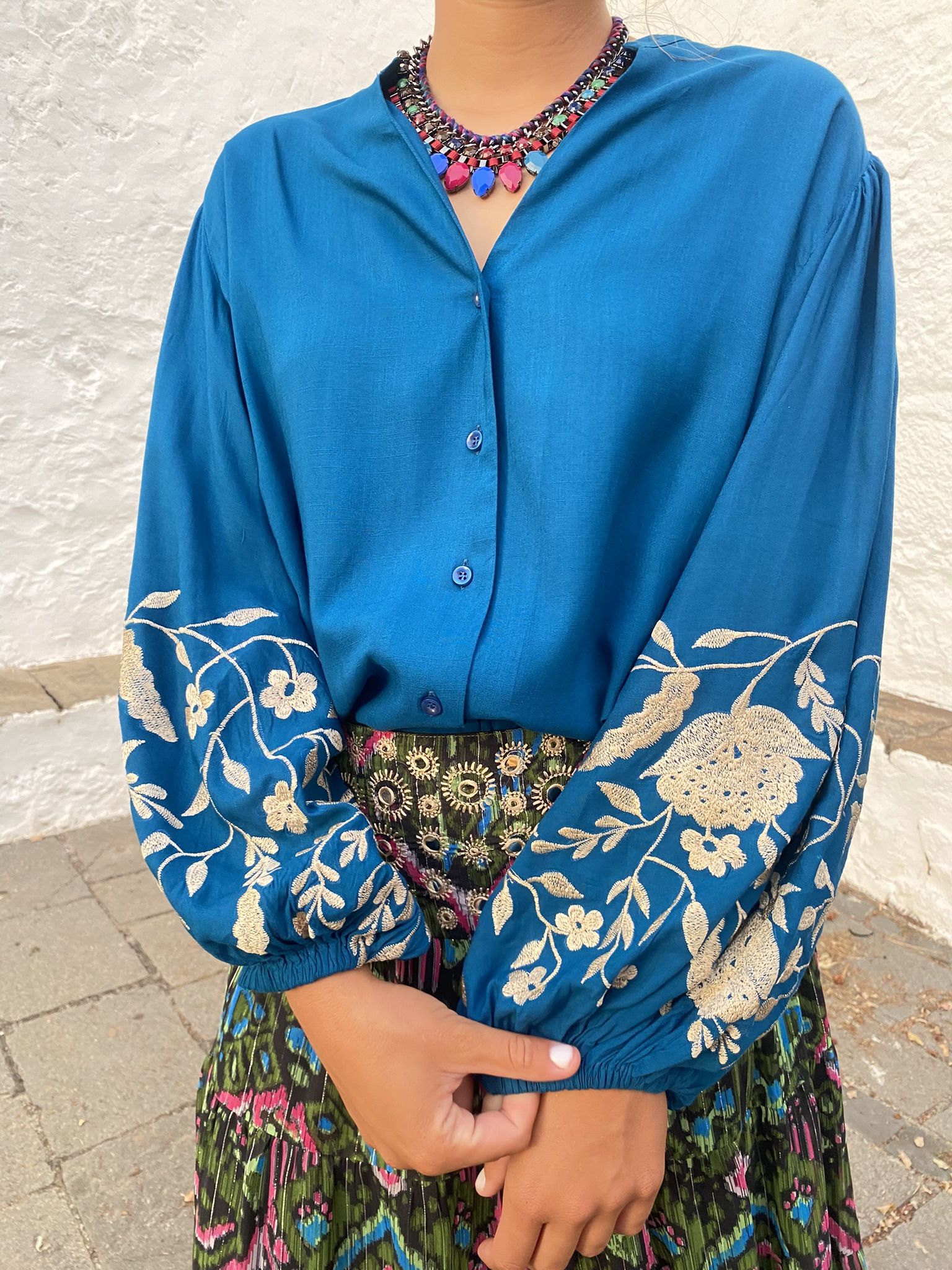 Blusa fluida de color azul, abotonada, de mangas globo largas, con bordados de flores en tono crudo