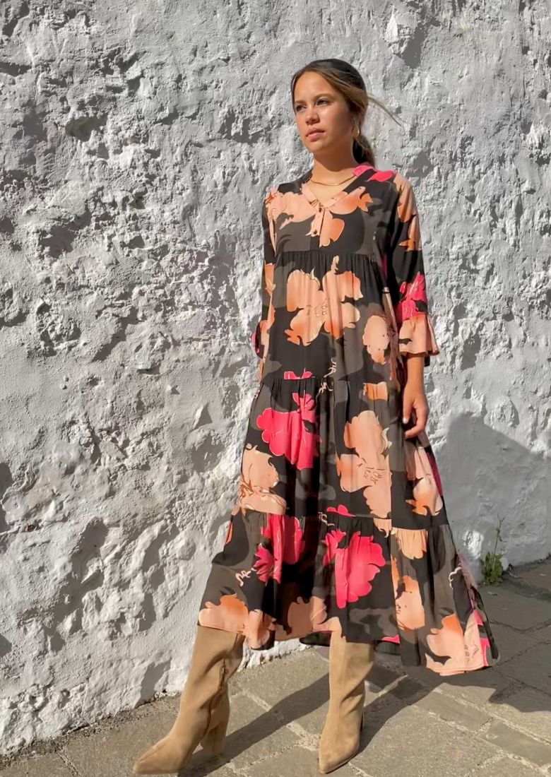 Mujer joven, parecida a Jennifer Lopez, con vestido largo de otoño, estampado, con fondo negro y colores rojo y tierras, fluido, de estilo boho chic