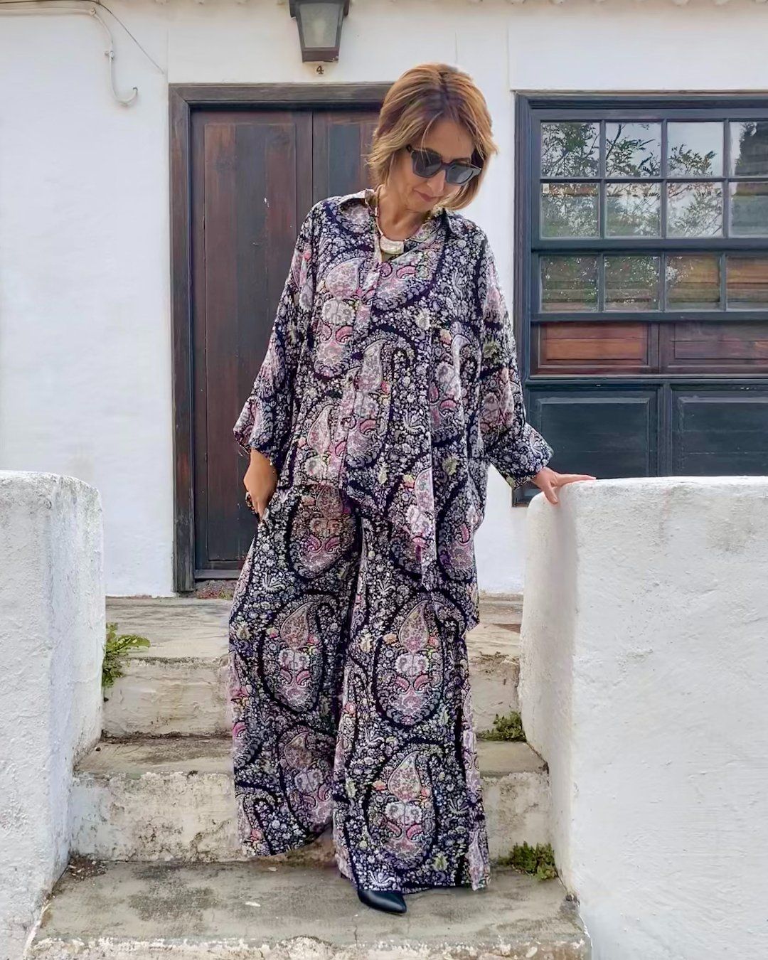 Mujer vestida con conjunto oversize de blusón y palazzo, con estampado de paisleys en tonos nude sobre negro, de esencia boho chic