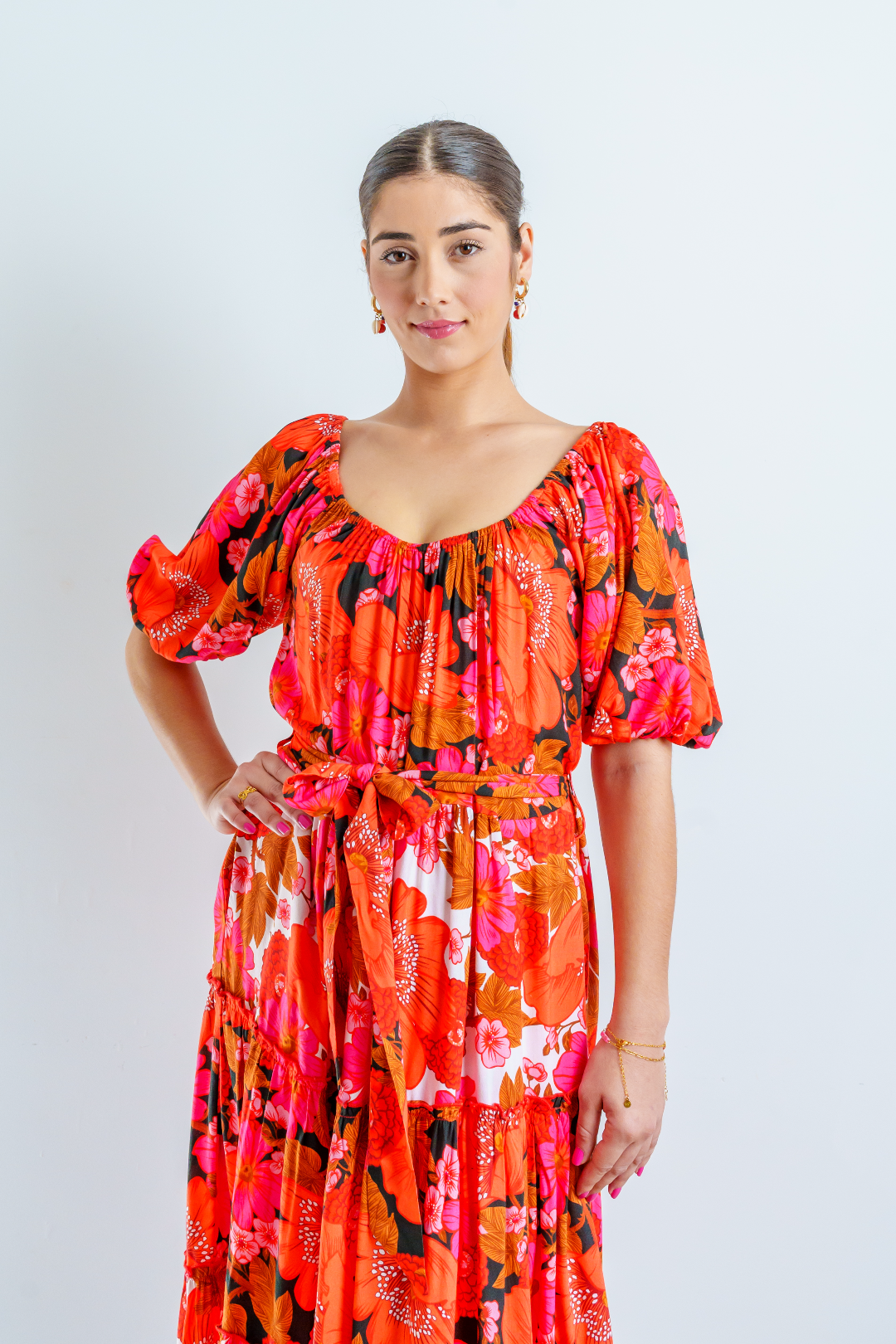 Imagen de medio cuerpo superior de mujer con vestido midi ANNA en estampado floral multicolor en tonalidades rojas, blancas, naranjas, fucsias y negra. Escote abarcado y mangas abullonadas.