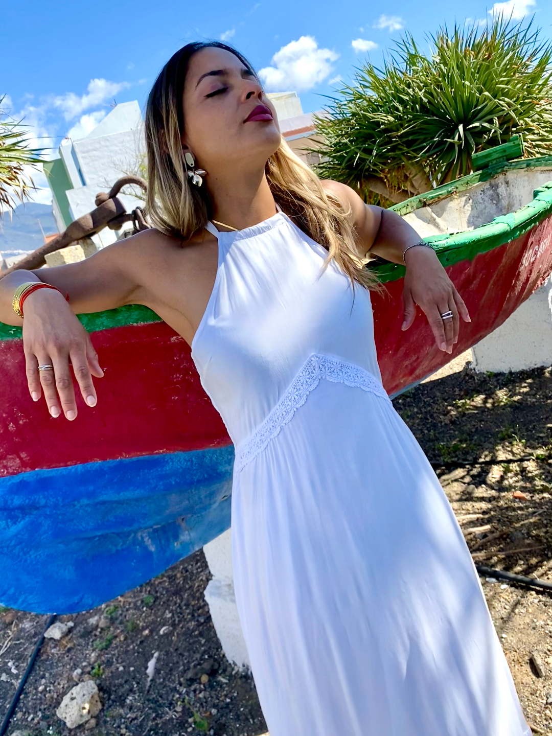 Mujer joven rubia con vestido largo blanco de estilo ibicenco boho chic, cuello Halter y espalda descubierta. Detalle del busto