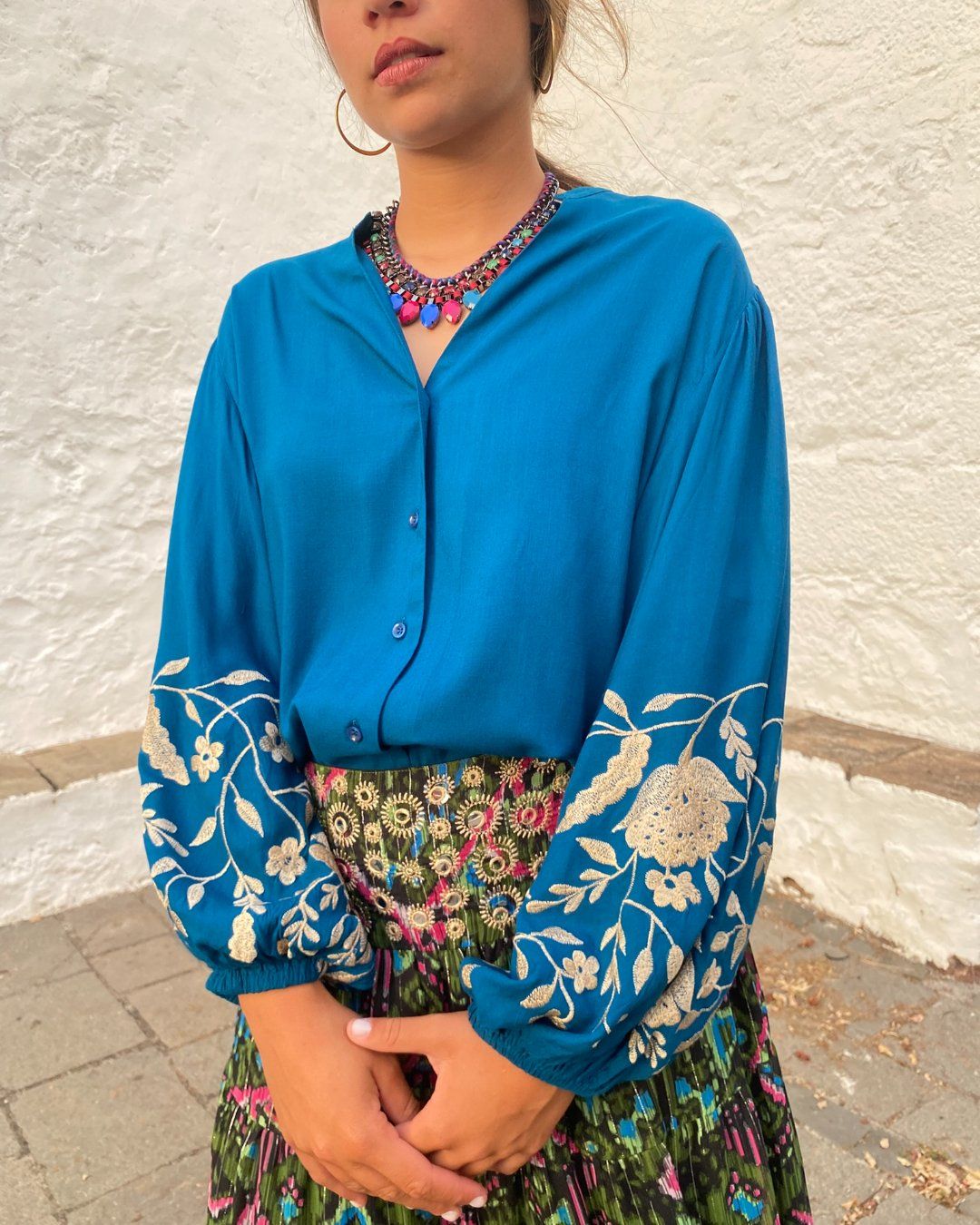 Blusa fluida de color azul, abotonada, de mangas globo largas, con bordados de flores en tono crudo