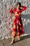 Mujer joven delante de pared blanca, vestida con vestido largo de otoño, en estampado en tonos rojos, de corte fluido, con vuelo y cinturón, de estilo bohemio, boho chic, de manga larga