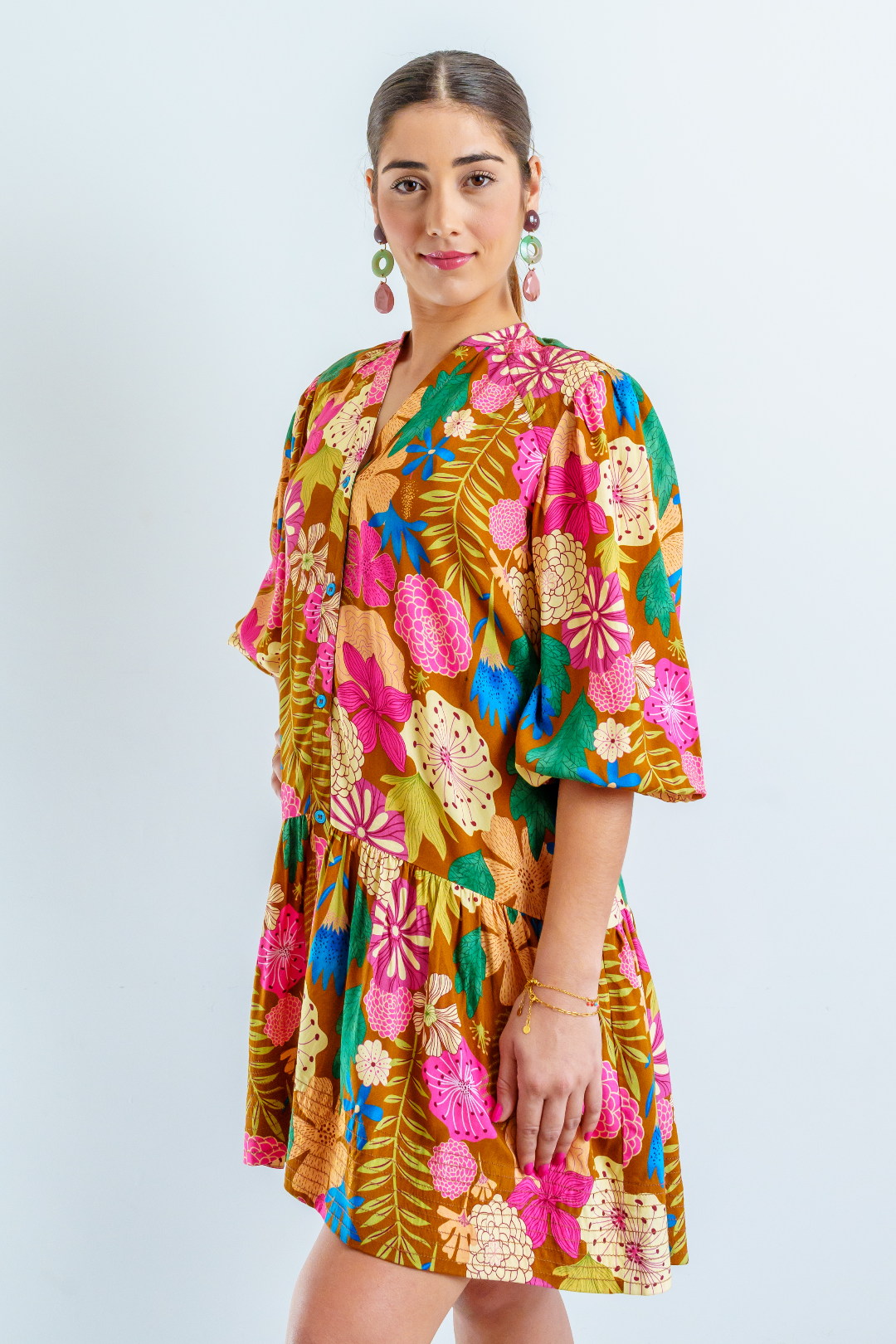 Imagen de medio cuerpo superior de mujer joven morena con vestido costo de estampado de flores grandes multicolor sobre fondo color caqui. El vestido es abotonado por delante, con cuello Mao y de corte suelto y fluido.