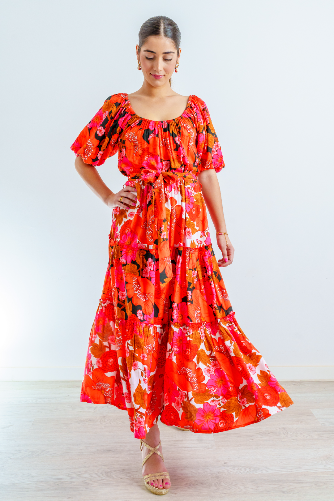 Mujer morena joven con vestido midi en estampado floral multicolor en tonalidades rojas, blancas, naranjas, fucsias y negra. Escote abarcado y mangas abullonadas.